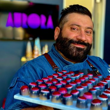 Headshot: Chef Nour holding a tray of chocolate bonbons against a blurry background.