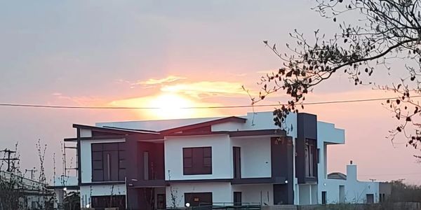 Modern house with sunset in the background and dry vegetation in front.