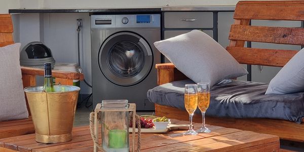 Cozy seating area with wooden furniture, wine, and snacks near a washing machine.