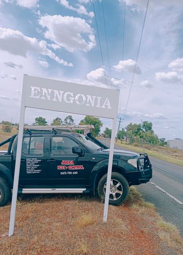 A pest control truck parked near an Enngonia town sign on a rural road.