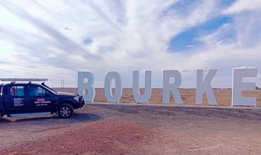 A black pest control vehicle parked beside large white letters spelling 'BOURKE' in an open field.