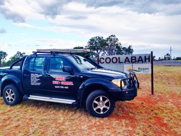 Black pest control truck parked near Coolabah sign on reddish grass.