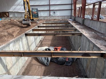 Construction site with a large rectangular pit and a yellow excavator.