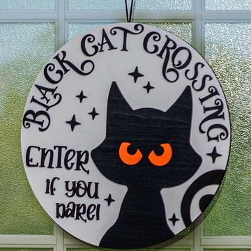 Round sign with a black cat silhouette and orange eyes, reading 'Black Cat Crossing Enter if you dare!'