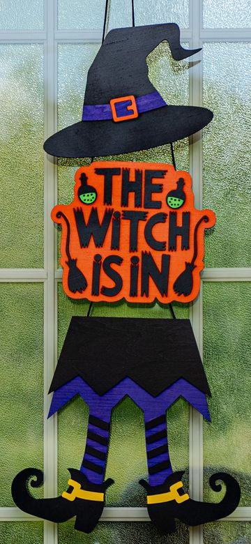 Halloween decoration saying 'The Witch Is In' with witch hat, skirt, and shoes.
