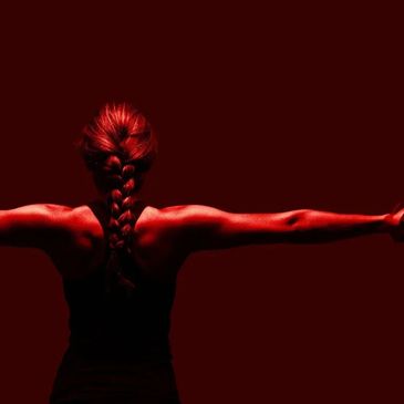 A woman with a braided ponytail seen from behind, arms stretched wide.