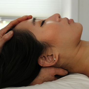 A woman receiving a gentle head and neck massage while lying down.
