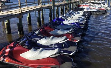 Row of Jet Skis on a dock with boats in the back