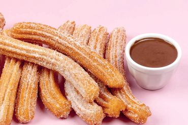 Sugar-coated churros with a cup of chocolate sauce on a pink background.