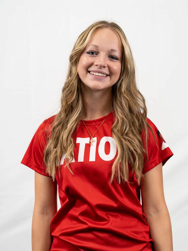 Young woman smiling in a red T-shirt with wavy blonde hair.
