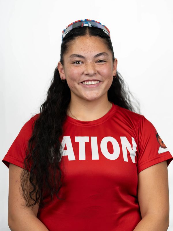 Smiling woman in a red shirt with long dark hair and sunglasses on her head.