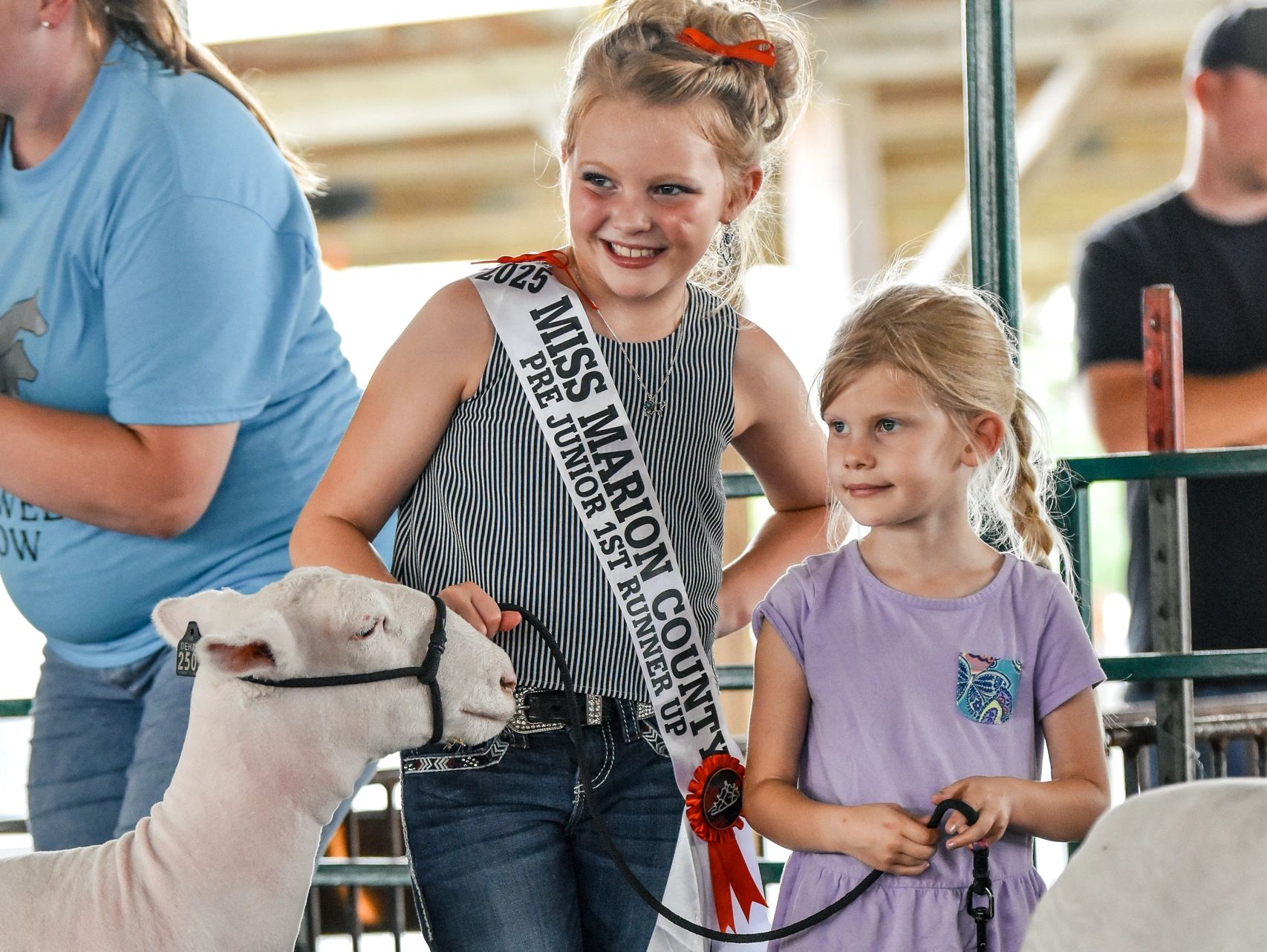 Two girls smiling with their sheep at a livestock event.