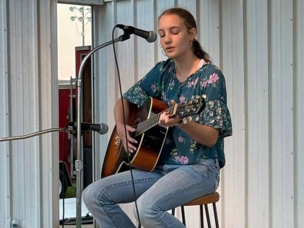 Young woman playing acoustic guitar and singing into a microphone.