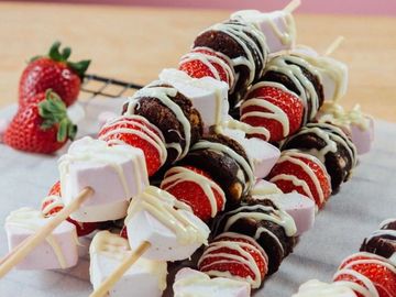 Colorful dessert skewers with strawberries, marshmallows, and chocolate drizzled with white icing.