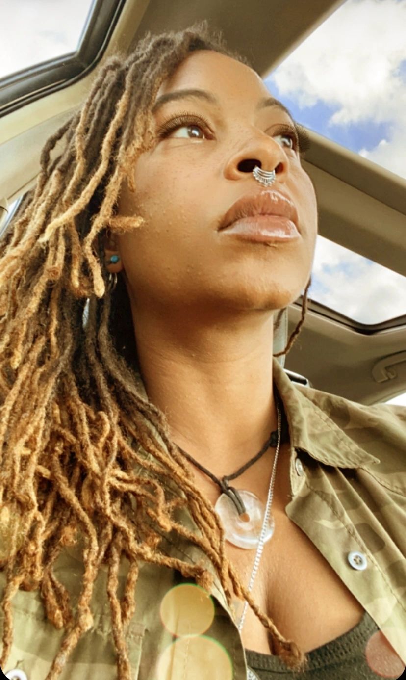 Woman with dreadlocks and septum ring looking out car window.