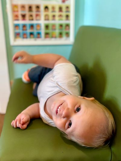 Happy toddler lying sideways on a green couch, smiling.
