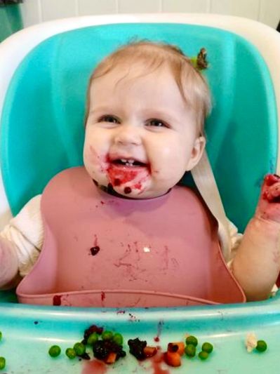 Smiling baby enjoying a messy meal with food on face and bib.