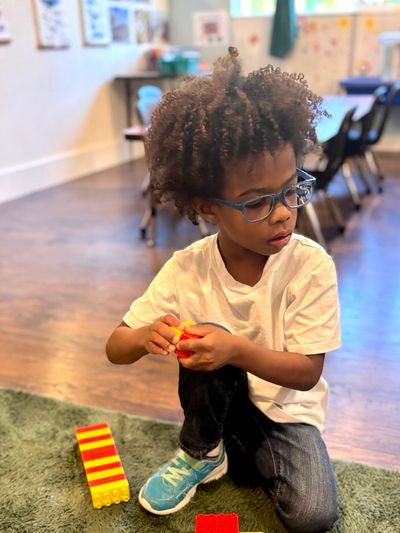 A child with glasses plays with building blocks on a green carpet.