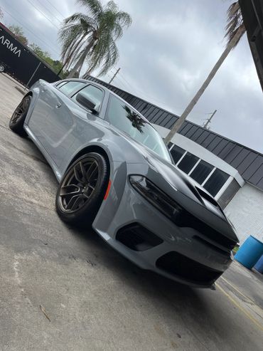 Sleek gray sports car with black hood and bronze wheels parked outdoors.