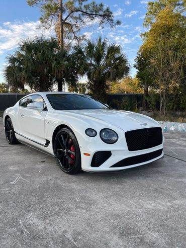 White Bentley Continental GT with black rims parked outdoors.