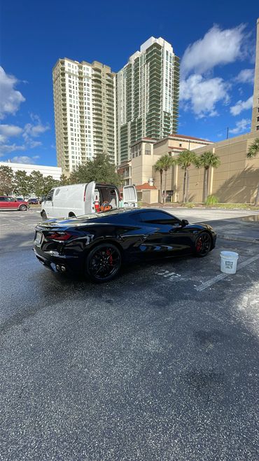 Sleek black sports car parked in an urban lot under a clear blue sky.
