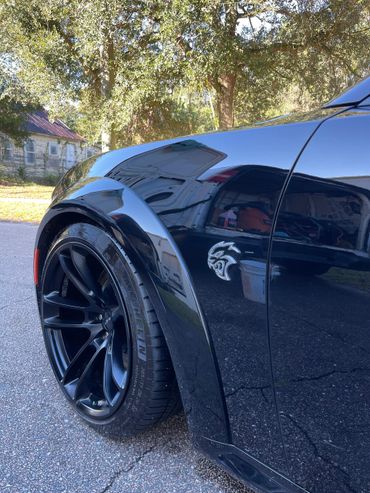 Close-up of a black car's rear wheel and Hellcat emblem.