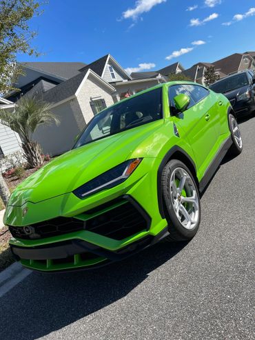 Bright green Lamborghini Urus parked on a sunny suburban street.