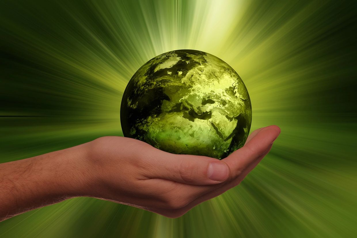 Hand holding a glowing green Earth with radiant light beams.