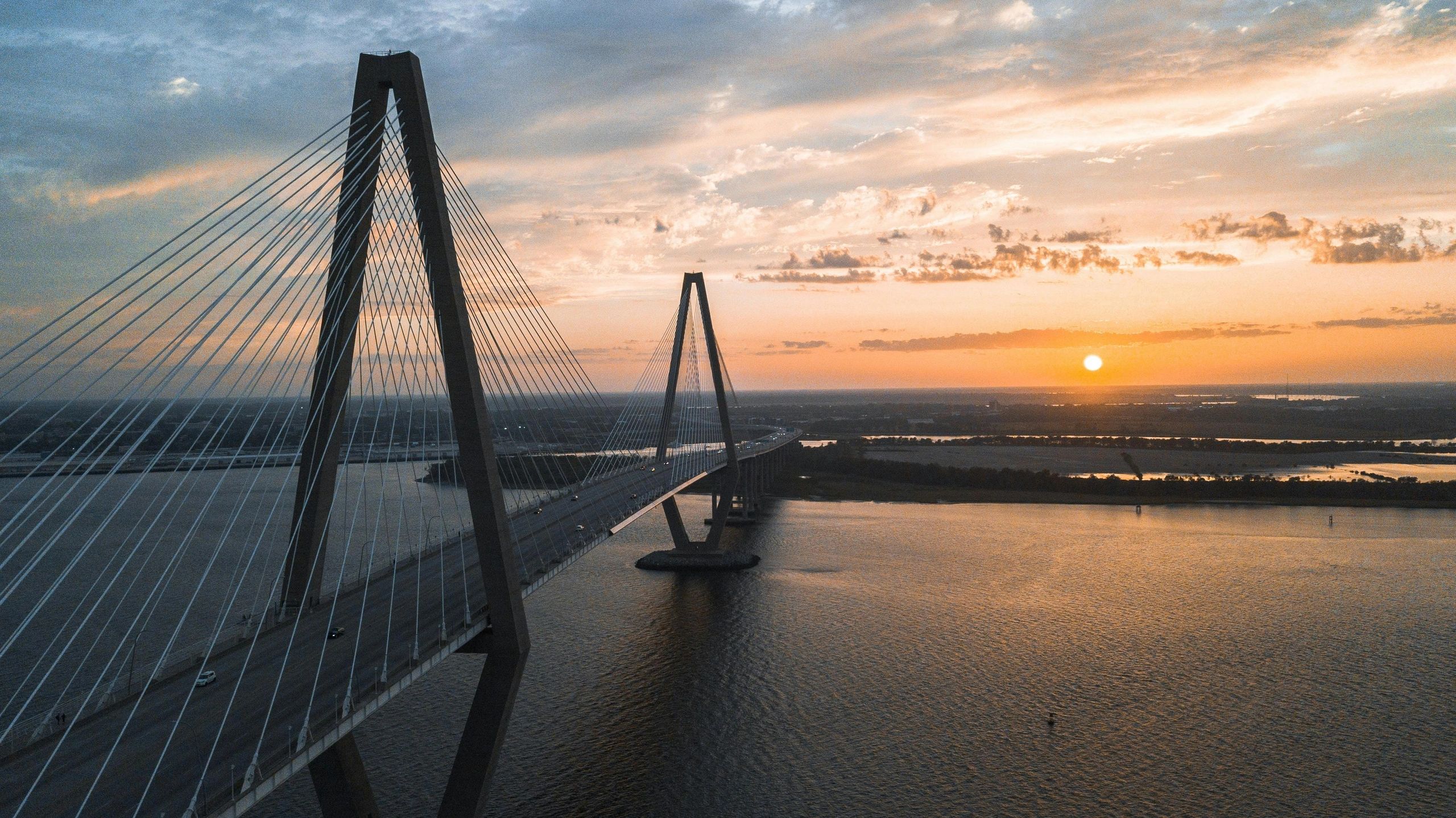 A cable-stayed bridge at sunset over a wide river.