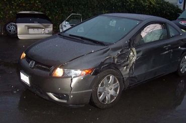A damaged gray Honda Civic with significant dents on the left side, parked in an area