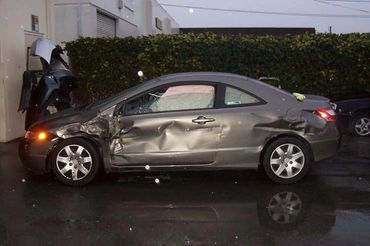 A gray sedan with significant damage to the driver's side, parked near a building