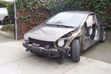 A stripped-down car with its front and side removed, parked on a driveway