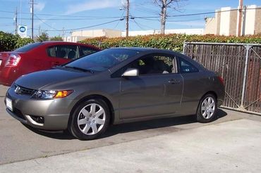 A gray Honda Civic coupe parked in a lot, with another red car in the background