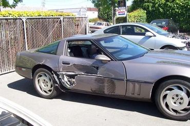A gray Corvette with significant damage to its driver's side door is parked in a lot