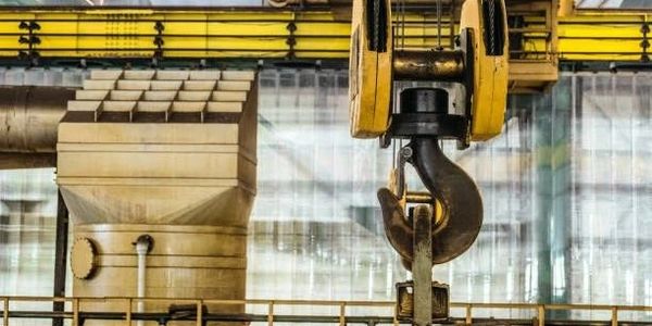 Close-up of a heavy industrial crane hook in a factory setting.