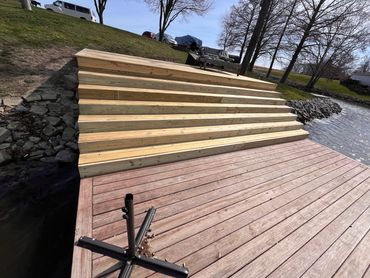 New wooden stairs connect a dock to a grassy hill beside a lake.