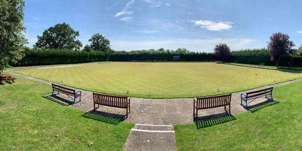 A well-maintained lawn bowling green with benches and clear skies.