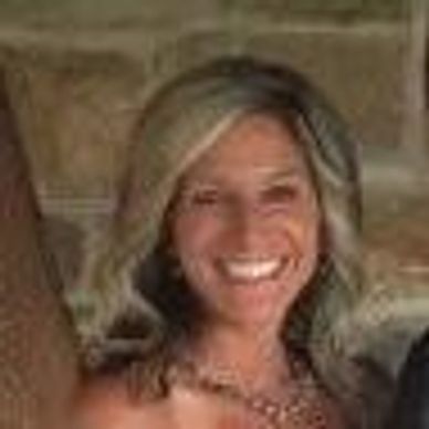 Smiling woman with blonde hair in front of a stone wall.