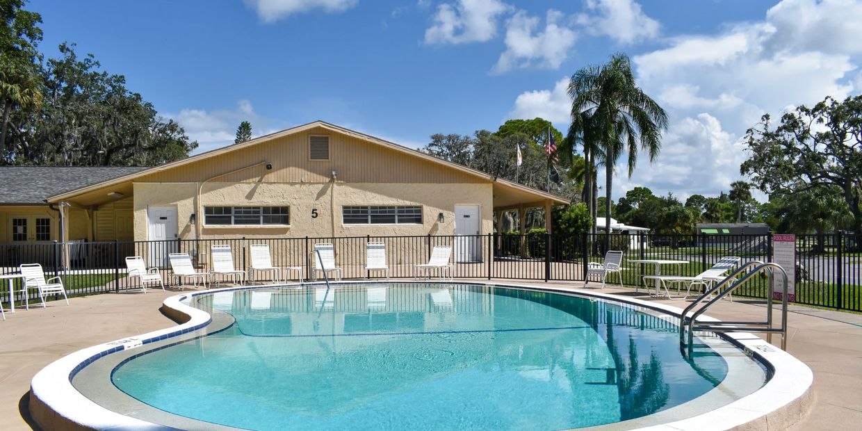 Outdoor swimming pool and clubhouse with lounge chairs at Oak Springs RV Resort in Port Richey, FL.