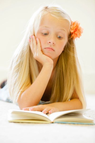 Young girl reading a book with a flower in her hair.