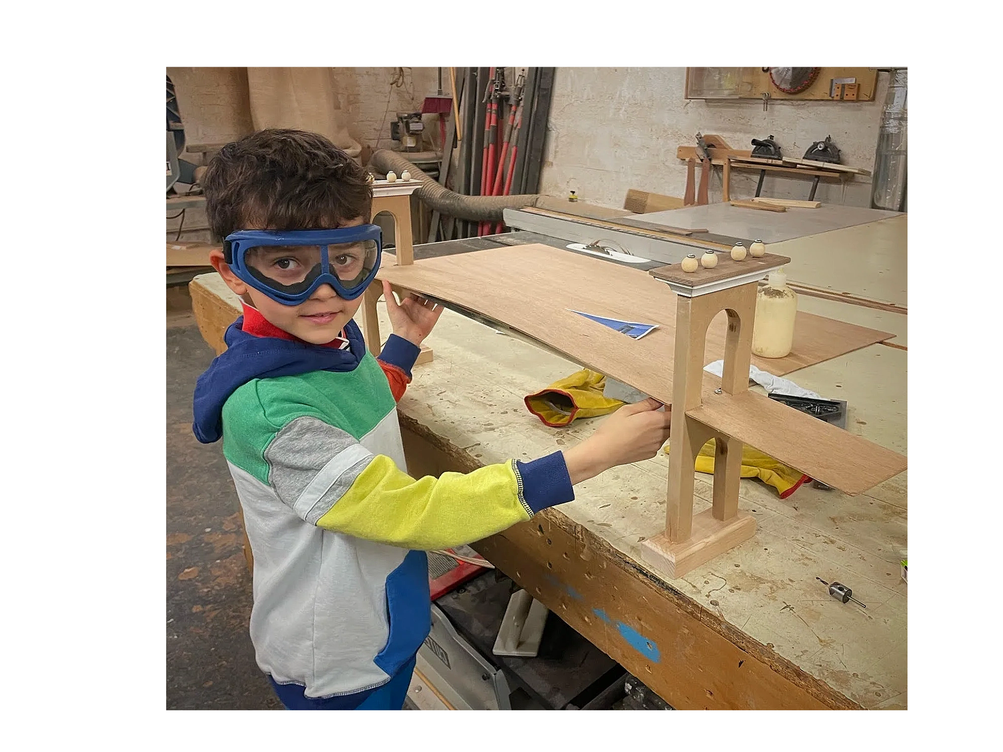 A kid dressed in bright colors works on building a 3 foot wooden Brooklyn Bridge replica