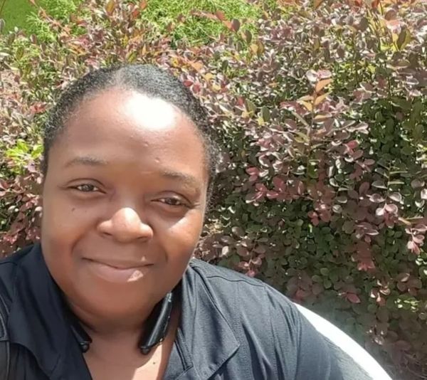 Woman smiling outdoors with greenery behind her.