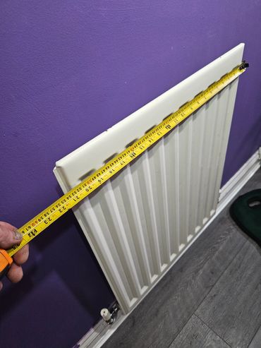 Measuring the width of a white radiator against a purple wall.