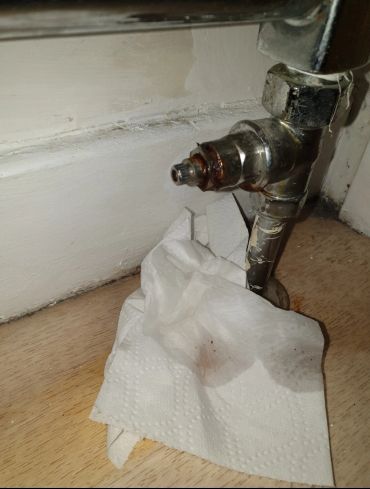 Rusty valve with stained paper towel on wooden floor.