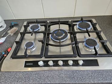 Gas stove with five burners lit and tools nearby.