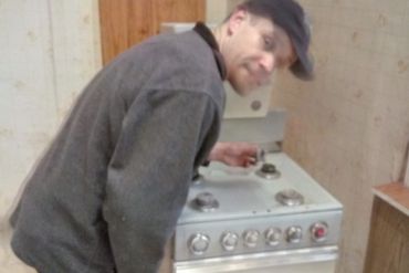 Man adjusting stove knobs in an old kitchen.