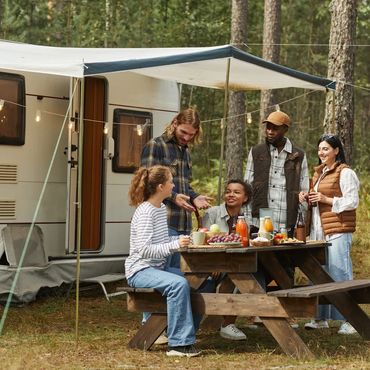 Friends enjoying a picnic by a camper in the woods.