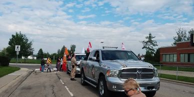 Parade vehicles and people on a street with flags.