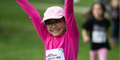 Smiling girl in pink raising arms at a race event.