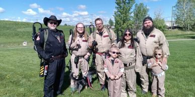 Group dressed as Ghostbusters posing outdoors on grass.